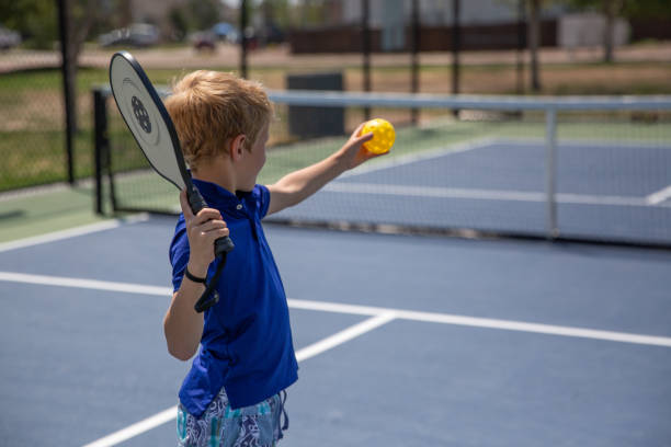 Young caucasian boy playing pickle ball on a hot summer day.